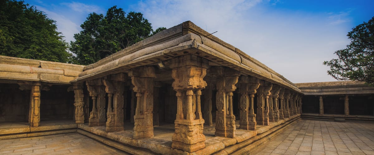 An ancient stone structure with columns and a flat roof, surrounded by trees and a clear sky.