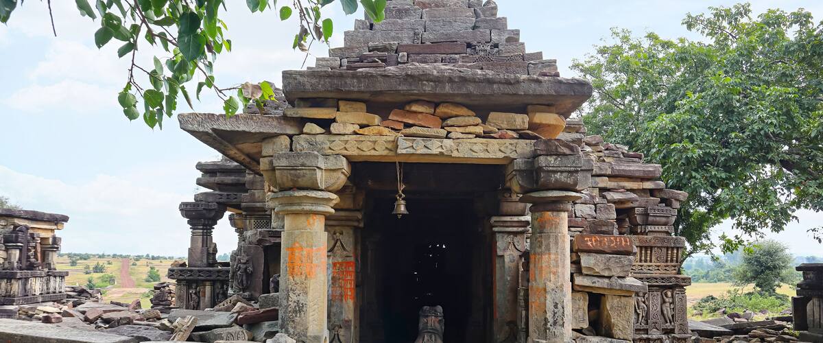 An ancient stone temple with intricate carvings and a large bell hanging from the entrance.
