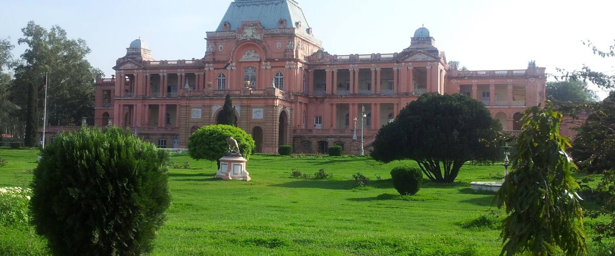 A large pink building with a dome and columns, surrounded by green lawns and trees.