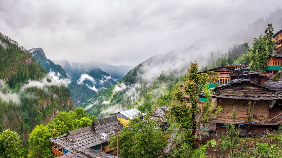 A mountainous village with traditional wooden houses, lush greenery, and mist-covered peaks.