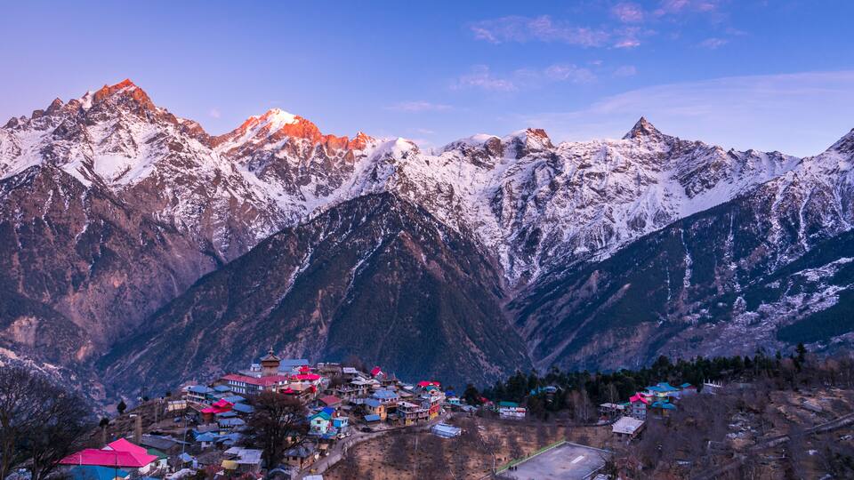 A mountainous landscape with snow-capped peaks and a village with colorful buildings at the base.