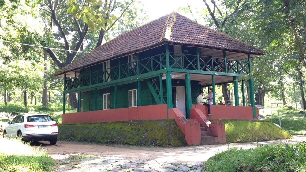 A green and red building with a tiled roof, surrounded by trees and a stone pathway.