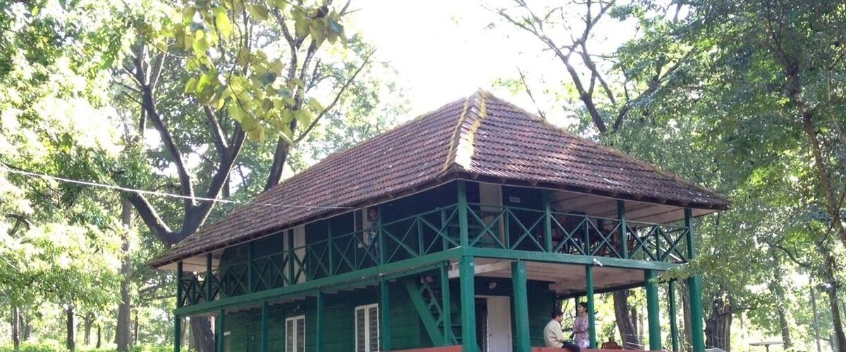 A green and red building with a tiled roof, surrounded by trees and a stone pathway.