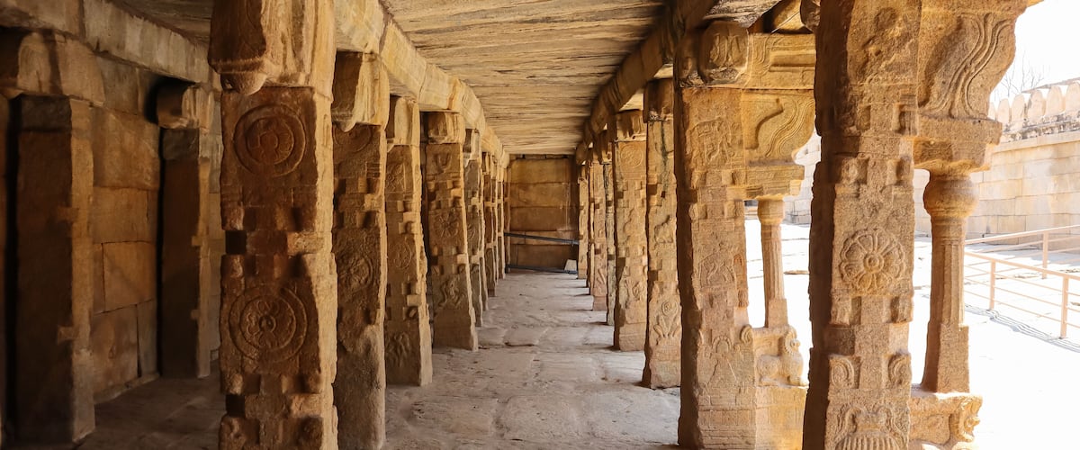 An ancient stone corridor with intricate carvings on the columns and walls.