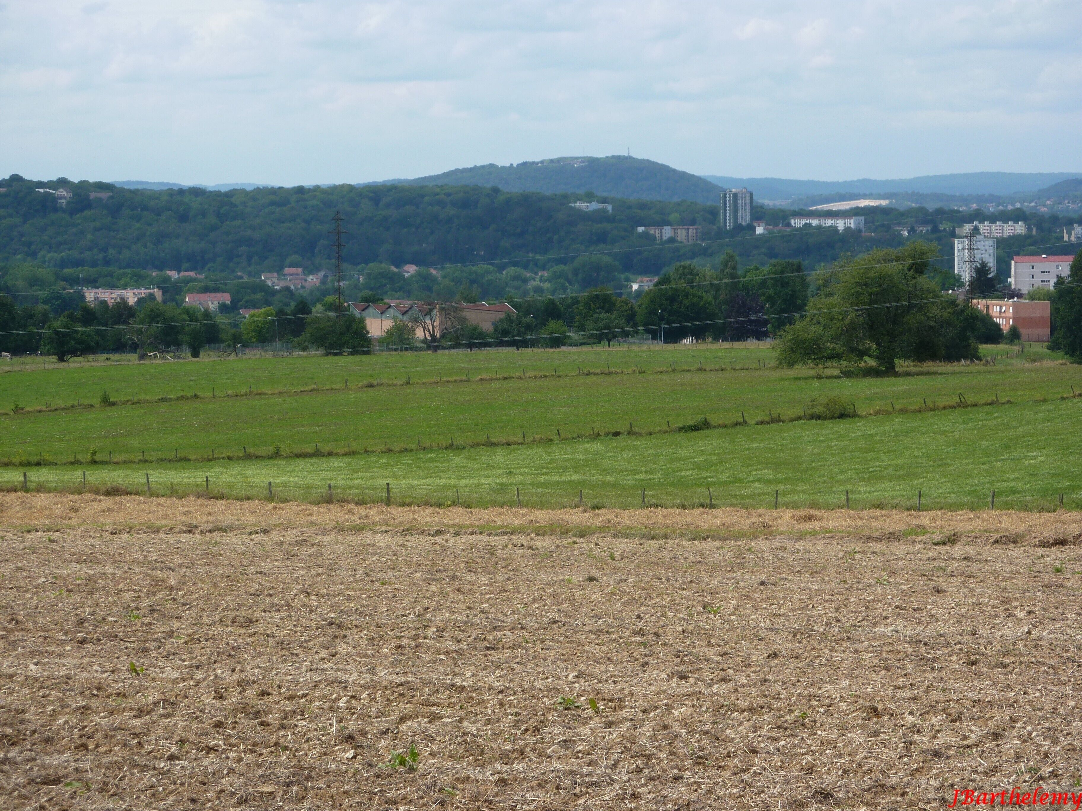 A rural landscape with fields, a hill, and buildings in the distance.