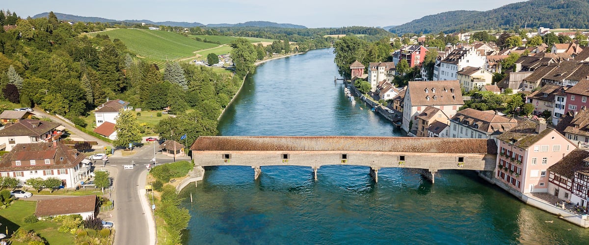 A river with a bridge, houses, and greenery.