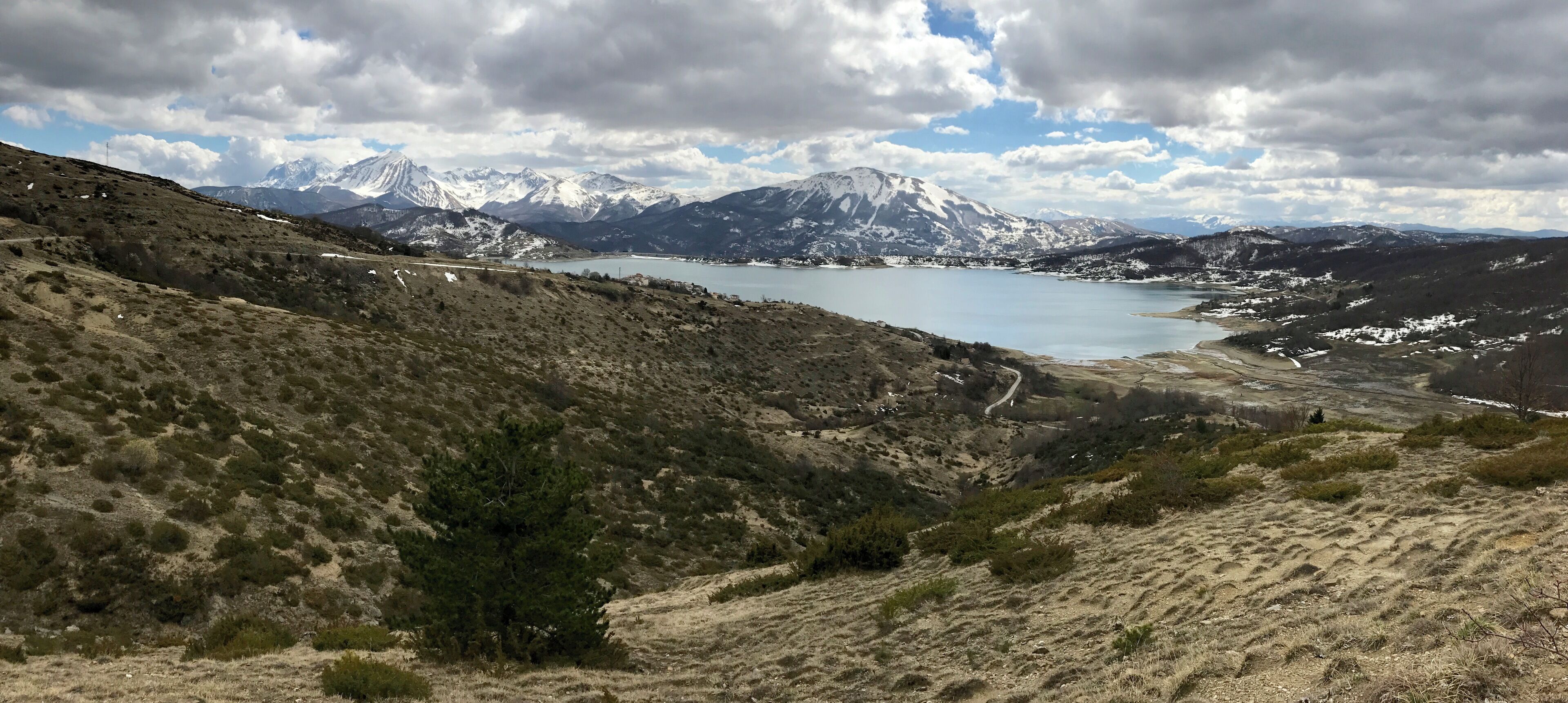 A mountainous landscape with a lake, snow-capped peaks, and sparse vegetation.