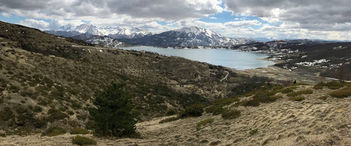 A mountainous landscape with a lake, snow-capped peaks, and sparse vegetation.