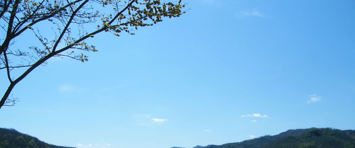 A calm lake surrounded by green hills and a clear blue sky.