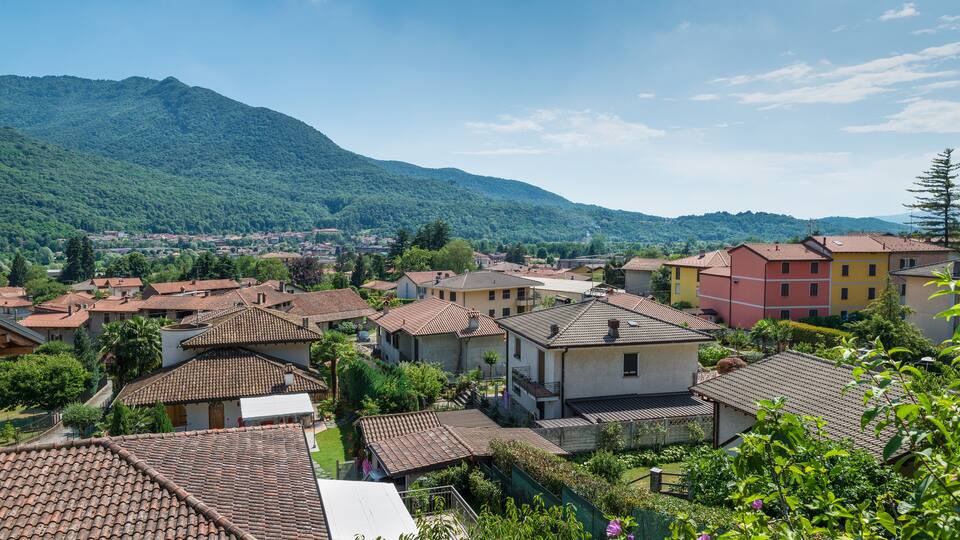 A village with terracotta-roofed houses, lush greenery, and a mountain in the background.