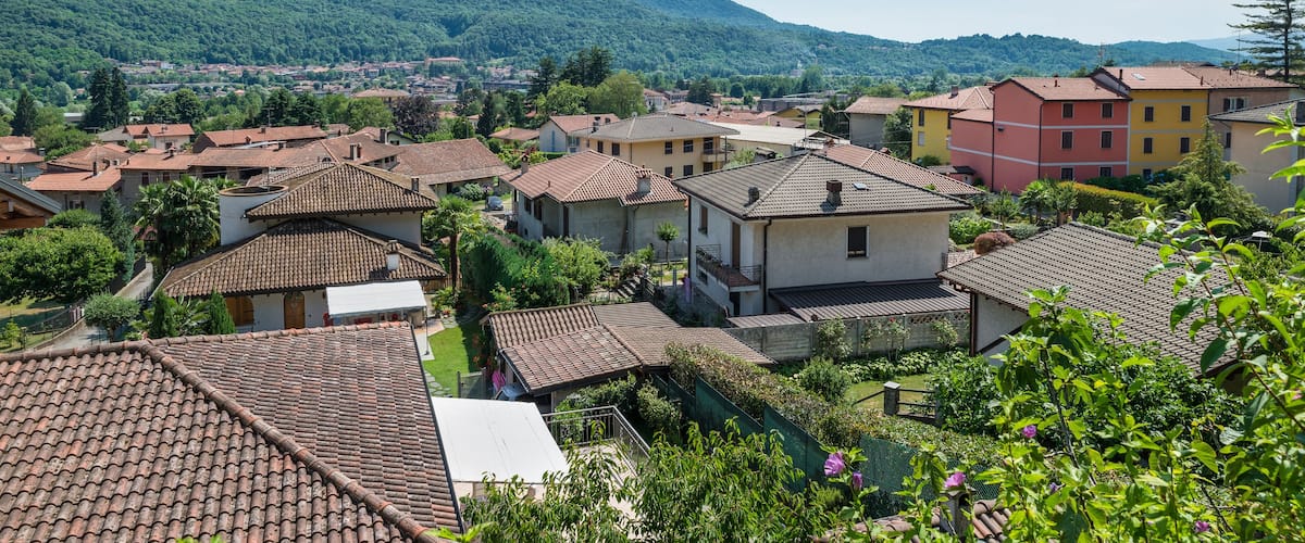 A village with terracotta-roofed houses, lush greenery, and a mountain in the background.