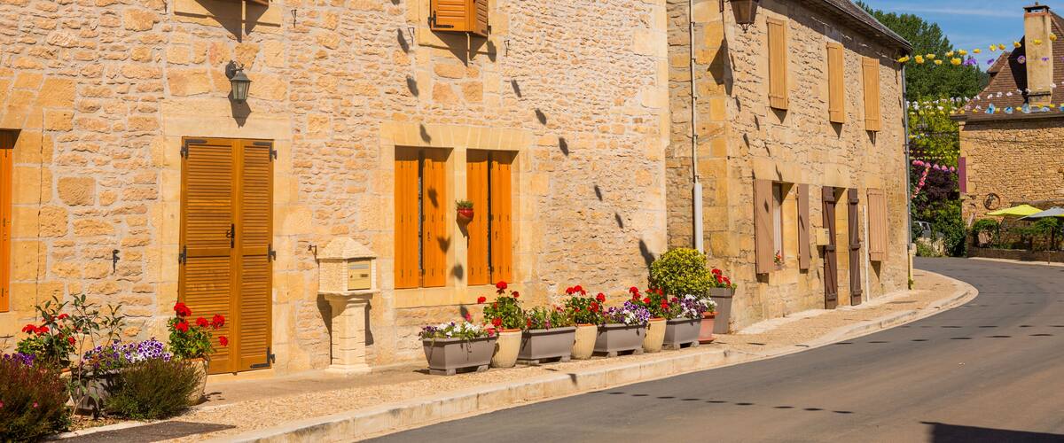 A stone building with wooden shutters and flower pots on the sidewalk.