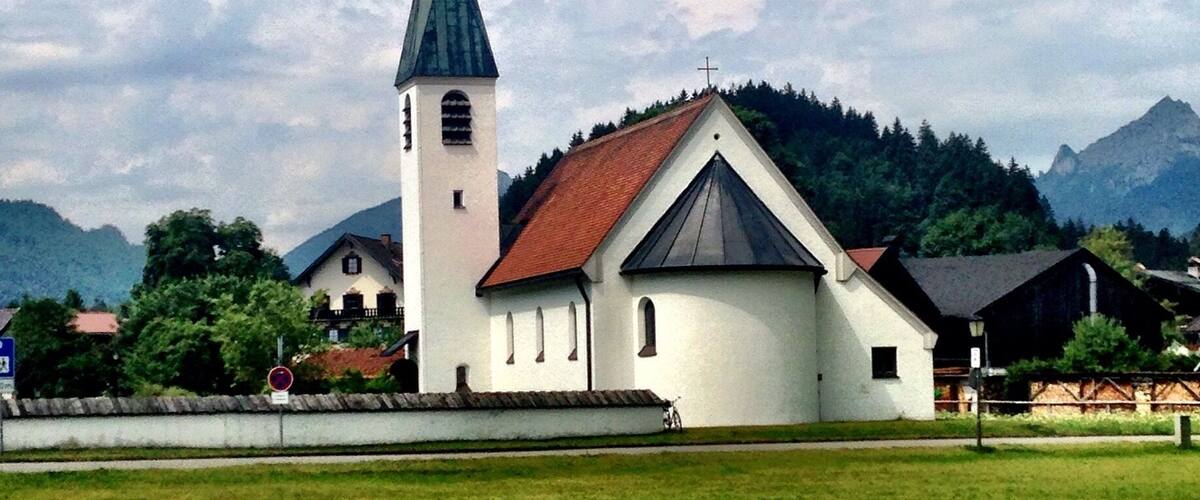 A church with a tall steeple and a red roof, surrounded by a green field and mountains in the background.