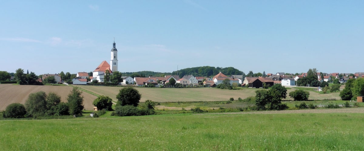 Ein ländliches Dorf mit einem markanten Kirchturm, umgeben von Feldern und Häusern.
