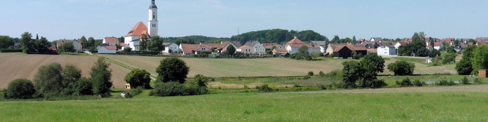 A rural village with a prominent church tower, surrounded by fields and houses.