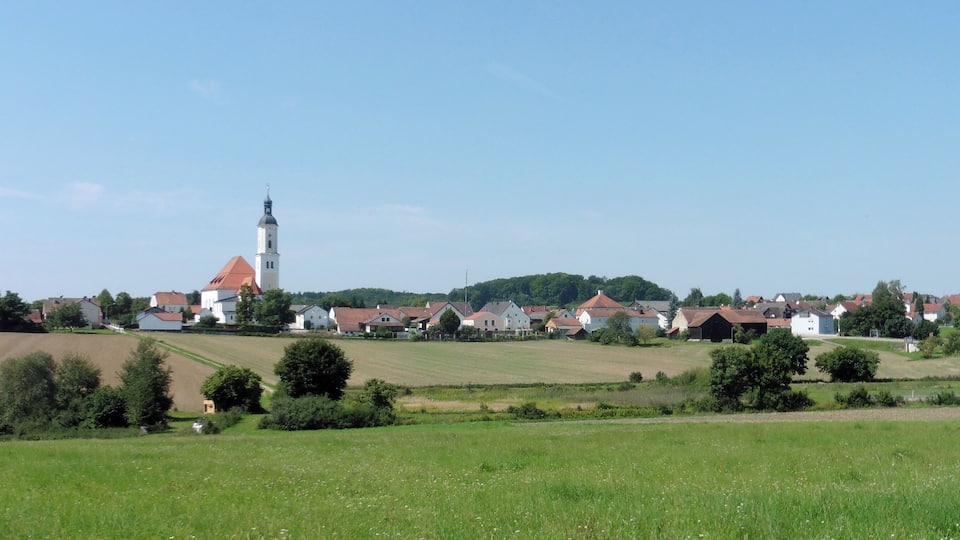 A rural village with a prominent church tower, surrounded by fields and houses.