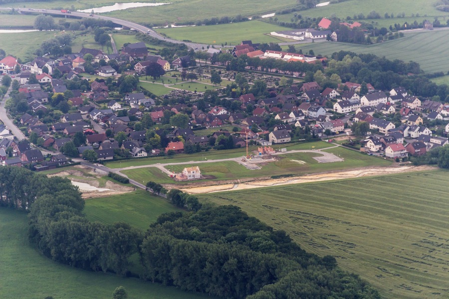 Vista aérea de un pueblo pequeño con casas agrupadas, campos verdes y algunos árboles dispersos.