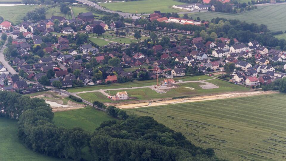 An aerial view of a small town with clustered houses, green fields, and a few scattered trees.