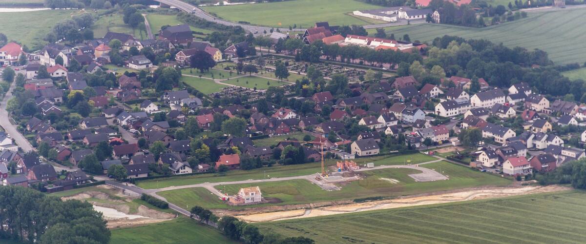 An aerial view of a small town with clustered houses, green fields, and a few scattered trees.