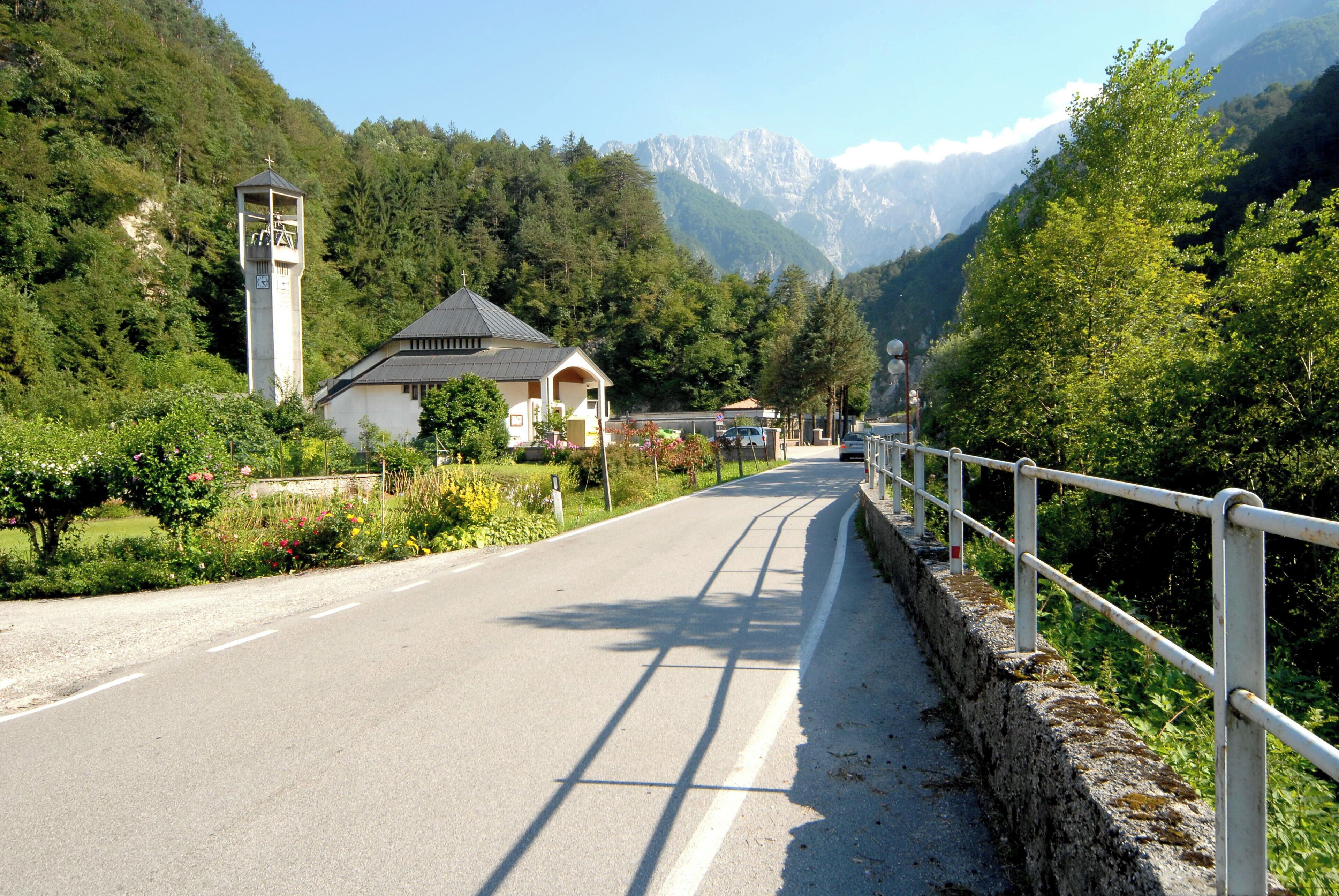 A road with a white fence, a church, and mountains in the background.
