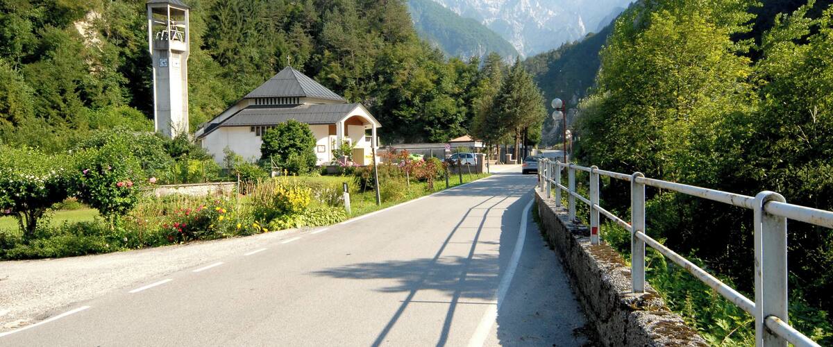 A road with a white fence, a church, and mountains in the background.