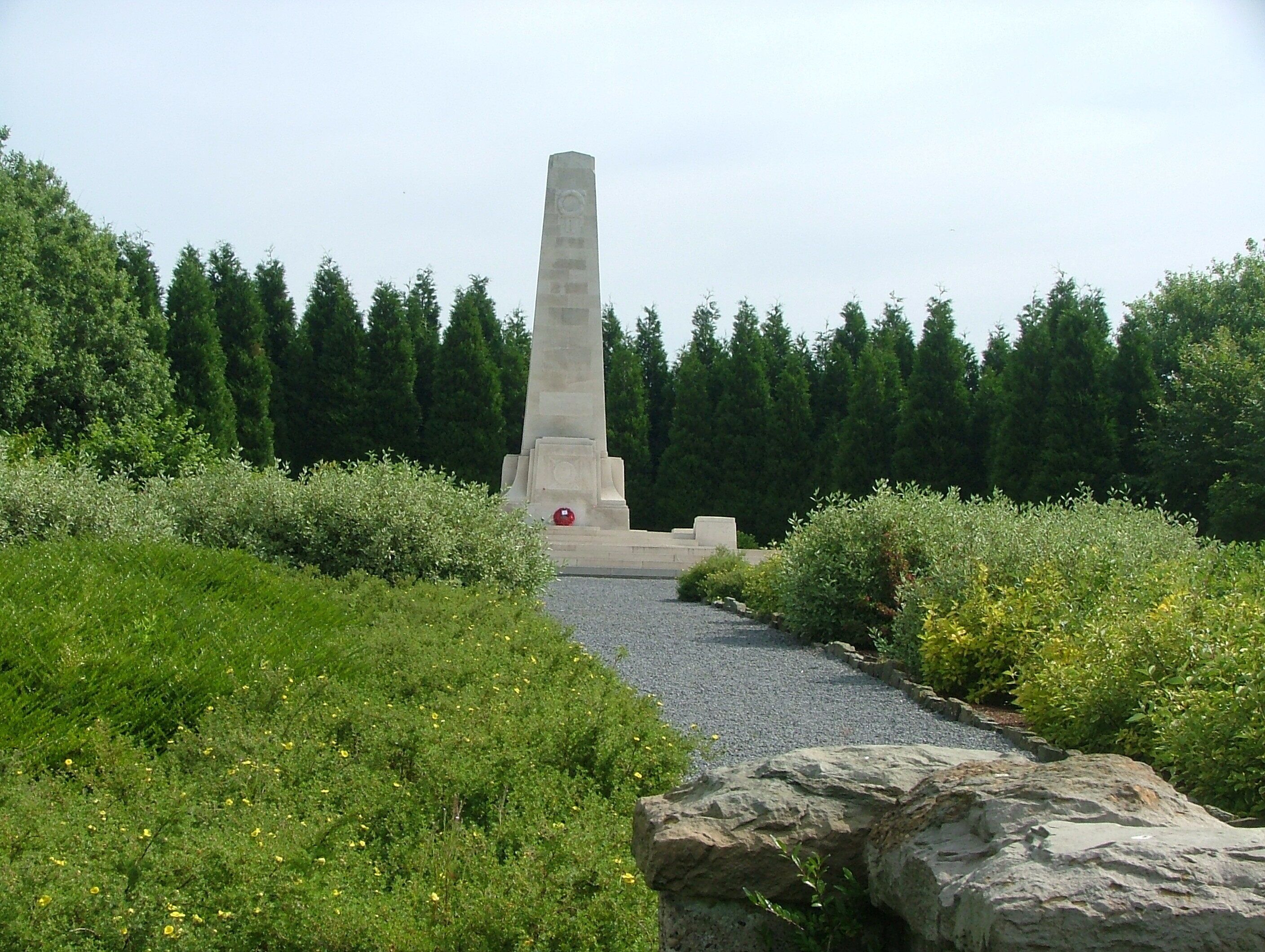 A tall monument surrounded by greenery and a gravel path.