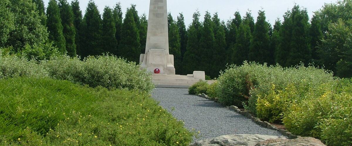 A tall monument surrounded by greenery and a gravel path.