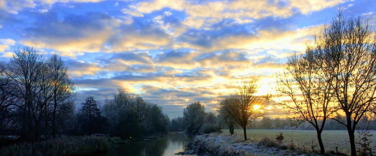 A river reflecting a sunset sky, surrounded by trees and frosty vegetation.