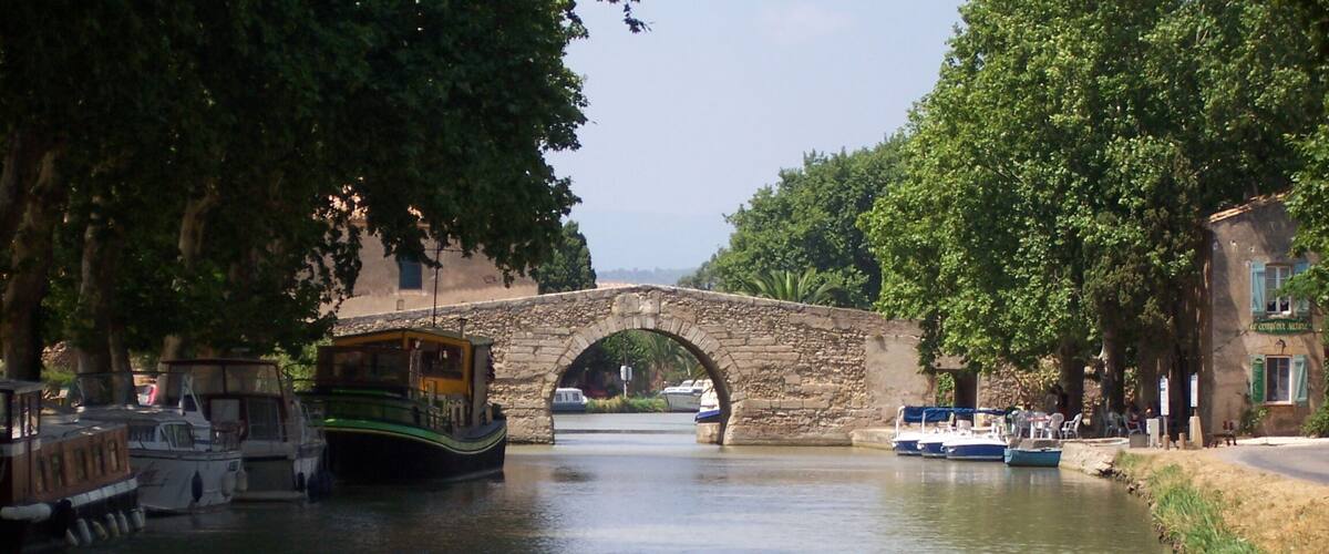 A stone bridge over a calm river, surrounded by trees and boats.