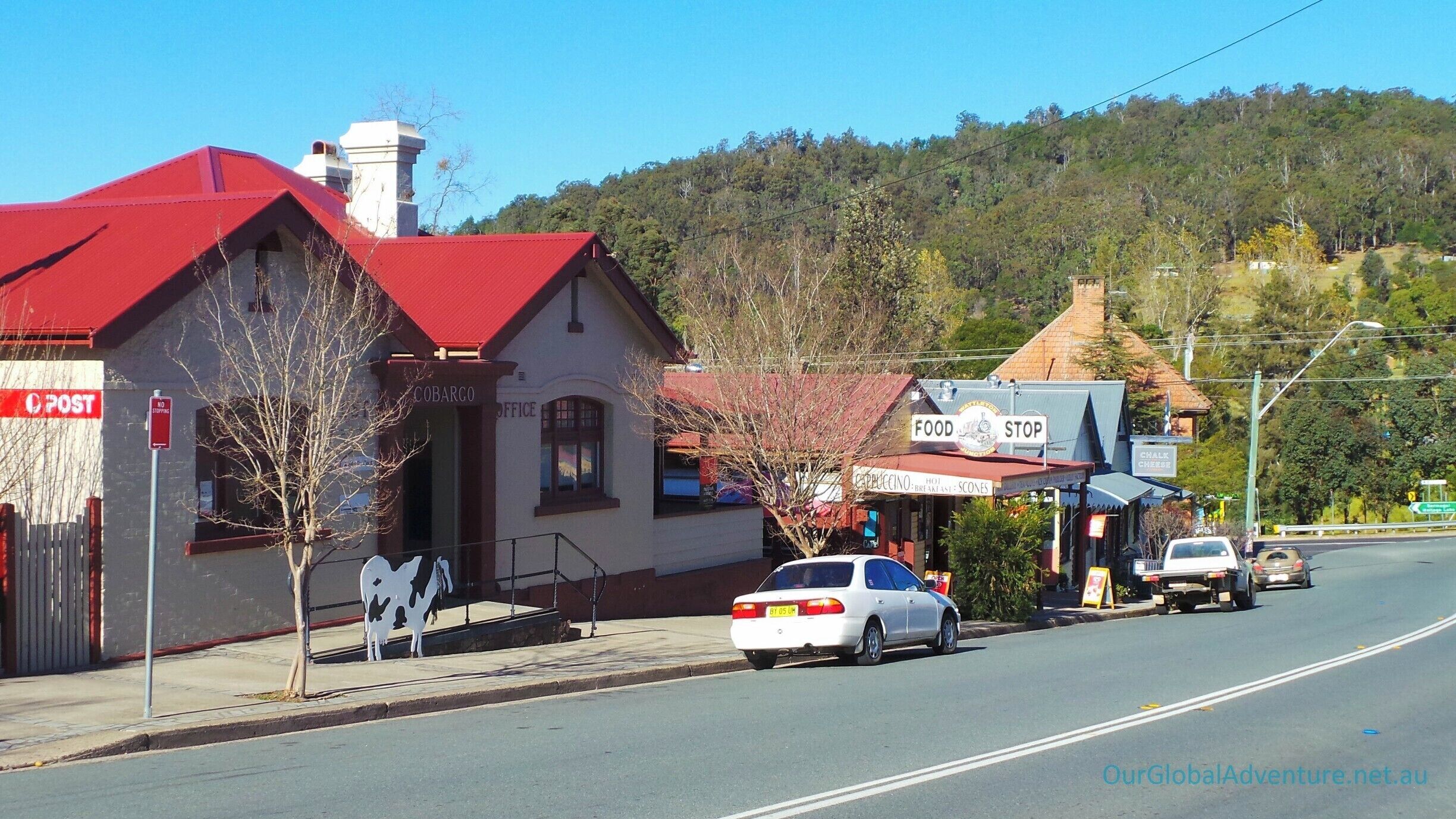A rural street with a red-roofed building labeled 'Cobargo Office' and a 'Food Stop' sign.