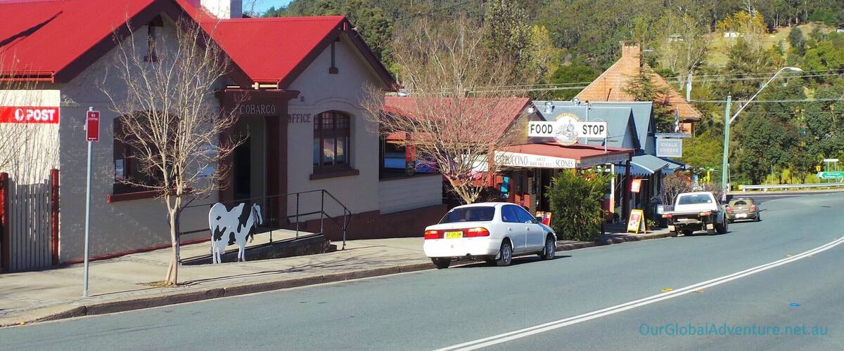 A rural street with a red-roofed building labeled 'Cobargo Office' and a 'Food Stop' sign.