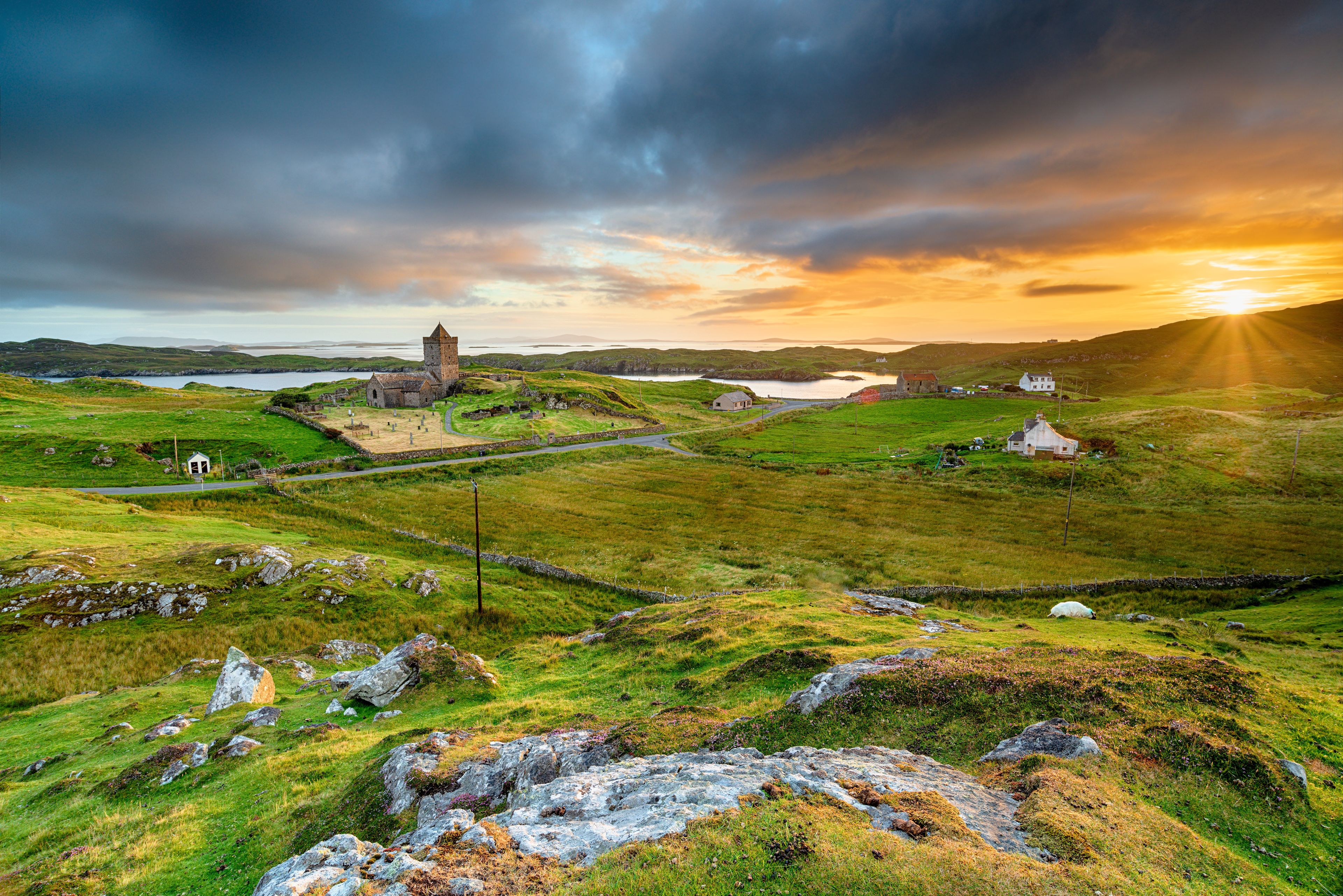 Un paysage côtier avec une église en pierre chargée d’histoire, des collines ondoyantes et un coucher de soleil.