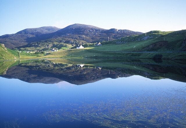 A calm lake reflecting a mountainous landscape with a small settlement.