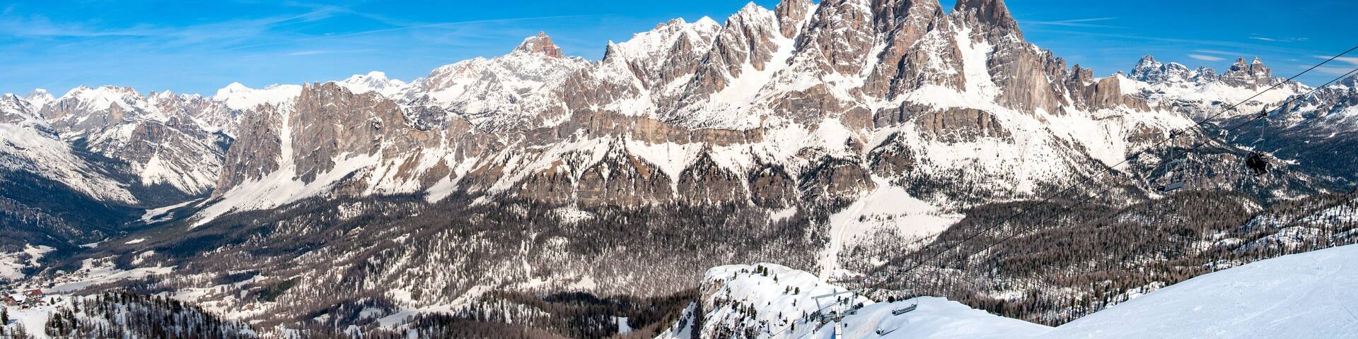 Snow-covered mountain peaks, a clear blue sky, and a ski lift in operation.