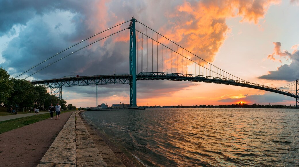 A suspension bridge over a river at sunset with a city skyline in the background.