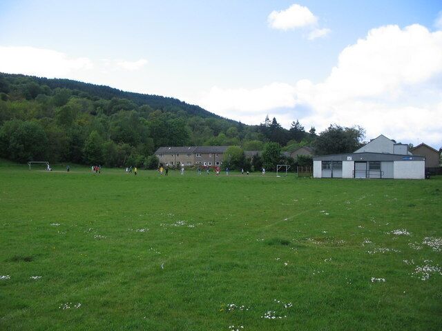 Fitba' in the park. A view looking to the northwest across the playing fields of Howie Park, with a football match in progress. The white building at right is the Princess Louise Memorial Hall, named after a relative of Queen Victoria and an erstwhile resident of Rosneath Castle.