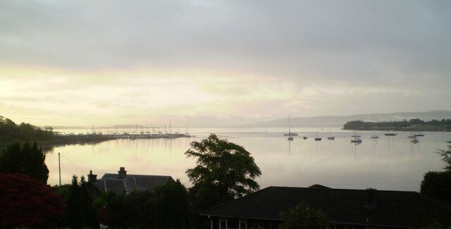 A calm lake with boats, a pier, and houses in the foreground.