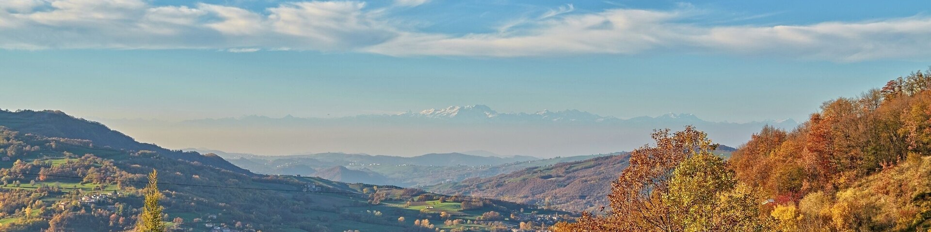 Paisaje montañoso con follaje otoñal, cielo despejado y cumbres nevadas a lo lejos.