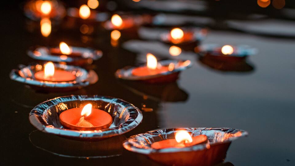 A row of lit candles in glass holders on a reflective surface.