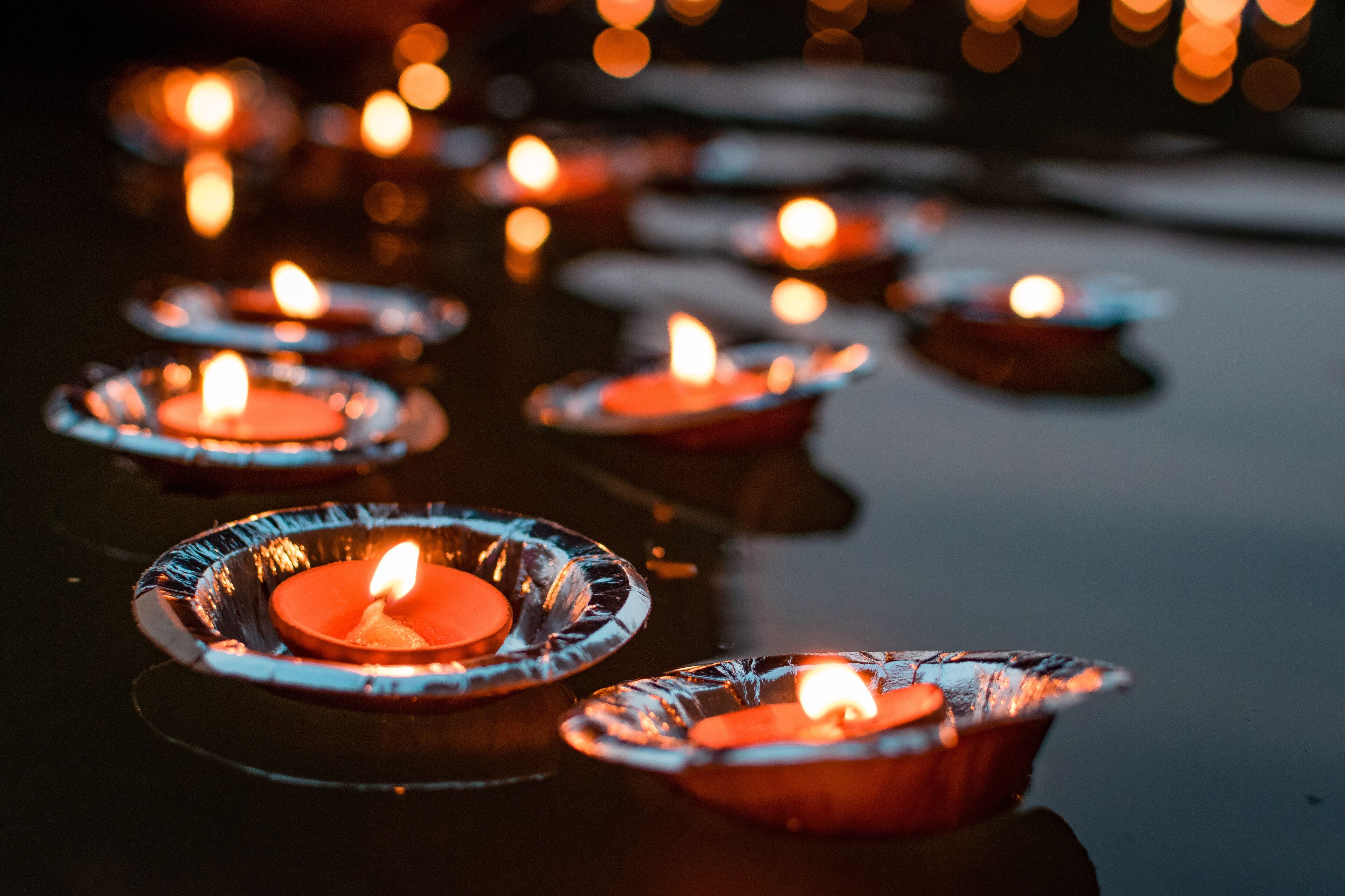 A row of lit candles in glass holders on a reflective surface.