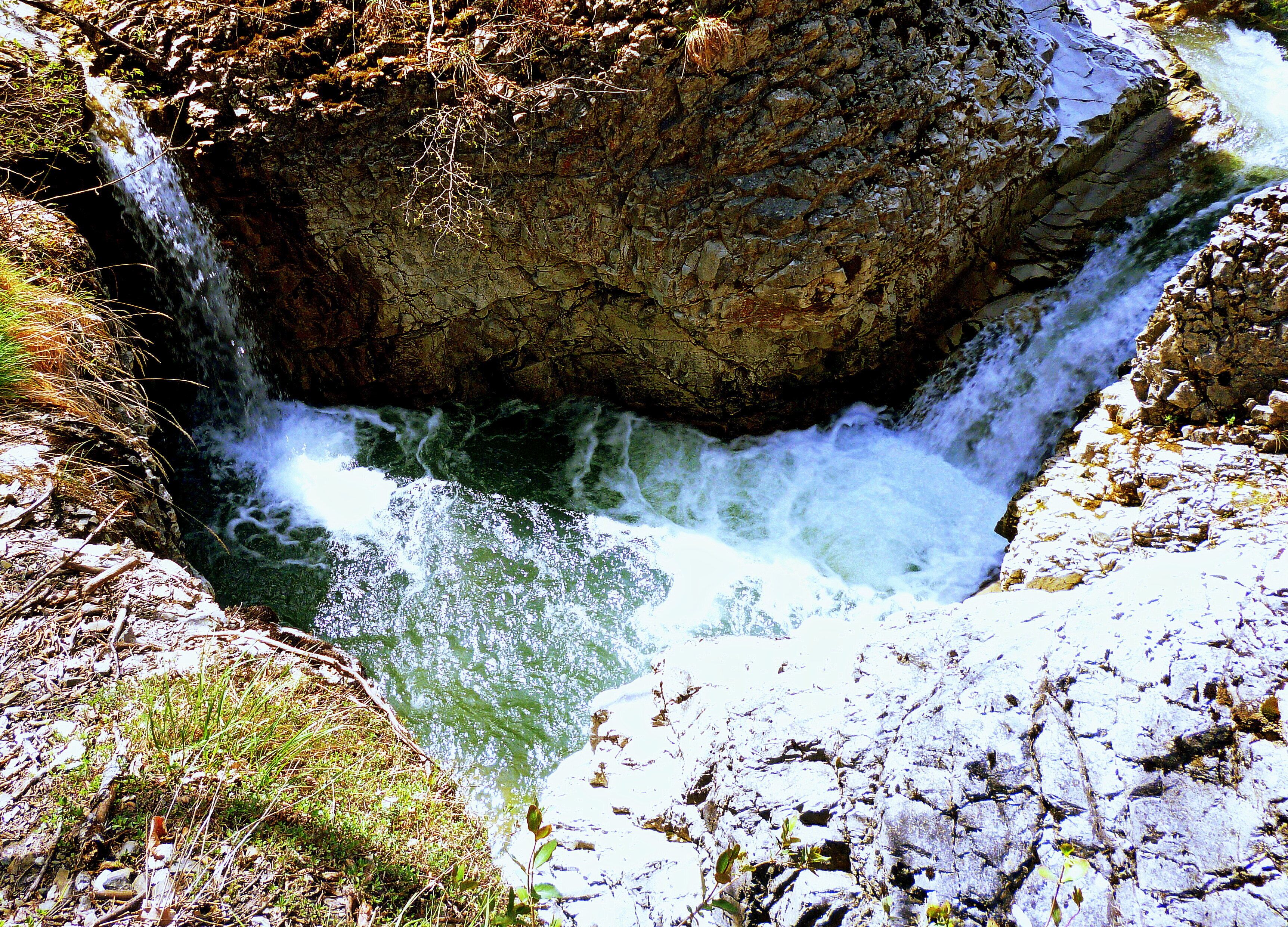 A waterfall cascading into a rocky gorge with sparse vegetation.