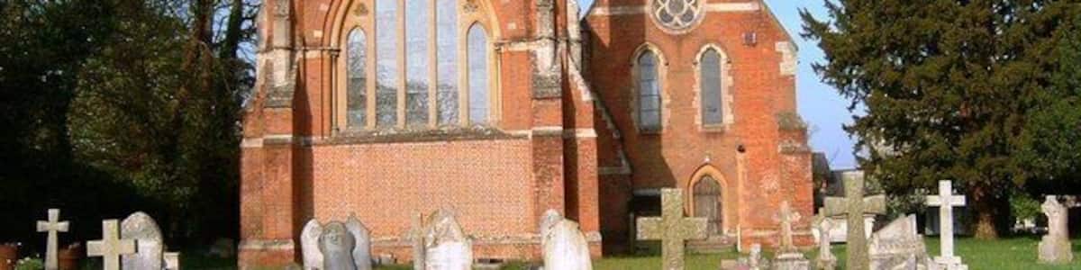 A church with a tall spire and a clock tower, surrounded by a cemetery with numerous gravestones.