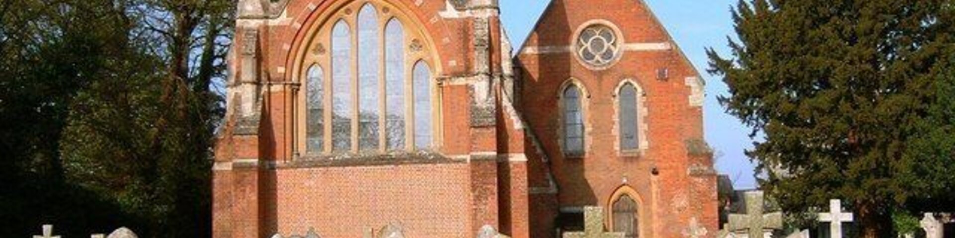 Una iglesia con una aguja alta y una torre del reloj, rodeada por un cementerio con numerosas lápidas.