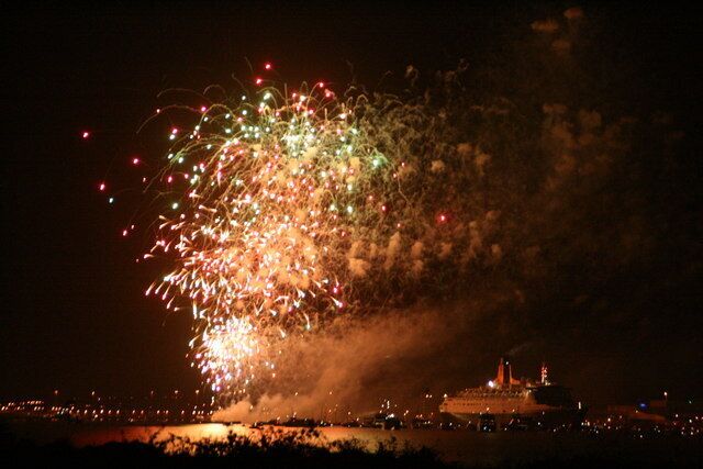 Um espetáculo de fogos de artifício à noite sobre uma paisagem urbana, com um edifício de destaque em primeiro plano.