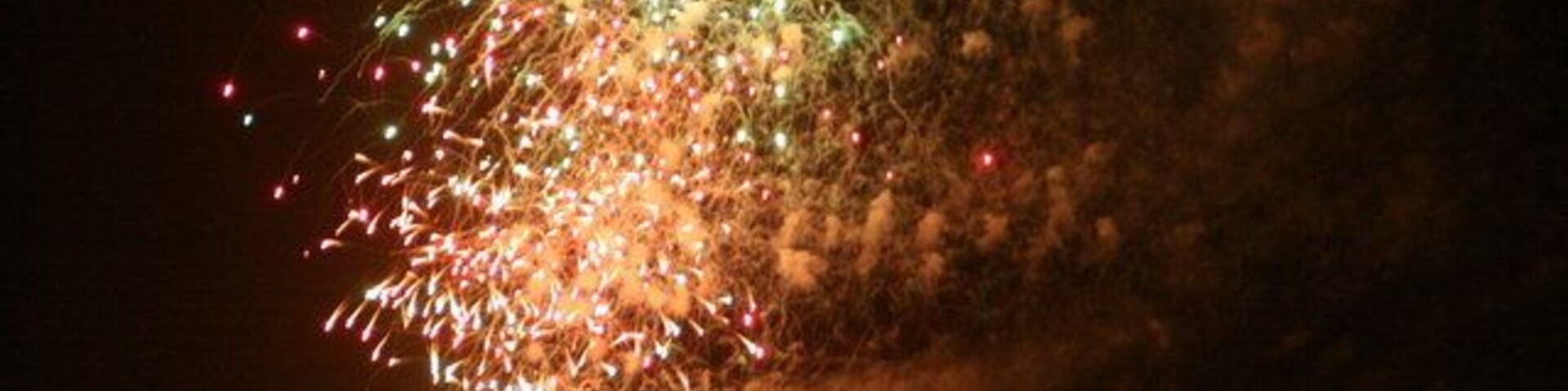 Um espetáculo de fogos de artifício à noite sobre uma paisagem urbana, com um edifício de destaque em primeiro plano.