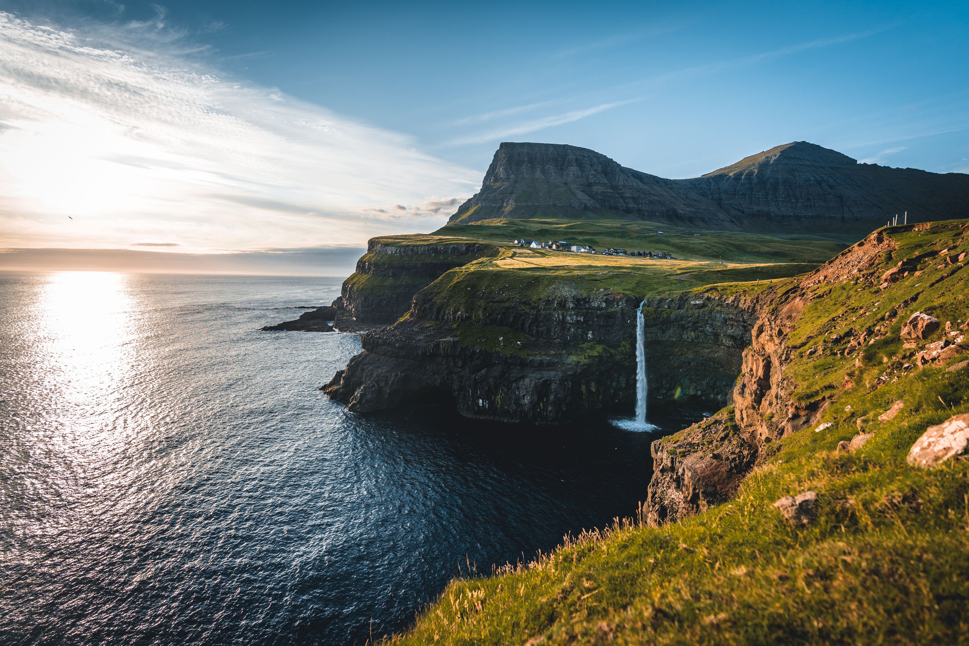 Gasadalur village and Mulafossur its iconic waterfall during summer with bluw sky. Vagar, Faroe Islands, Denmark. Rough see in the north atlantic ocean.