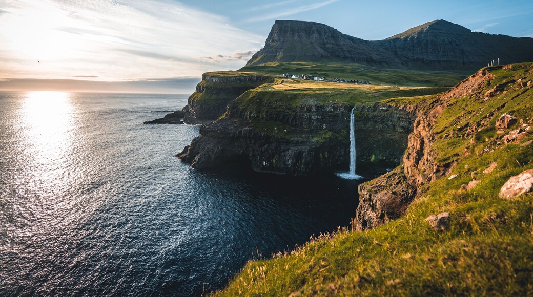 Gasadalur village and Mulafossur its iconic waterfall during summer with bluw sky. Vagar, Faroe Islands, Denmark. Rough see in the north atlantic ocean.