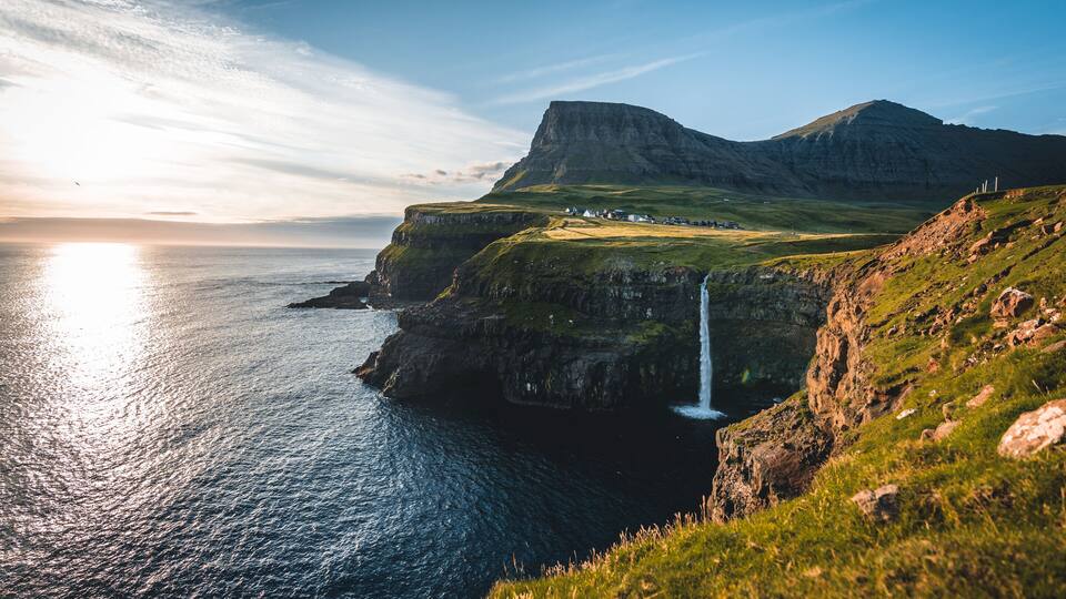 A coastal landscape with a waterfall, cliffs, and a sunset.
