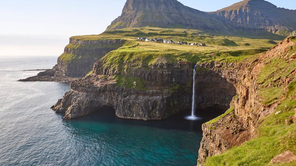A coastal landscape with a waterfall, green hills, and a small settlement.