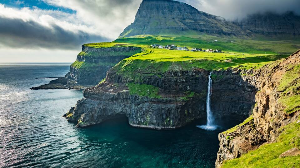 A coastal landscape with a waterfall, green cliffs, and a village.
